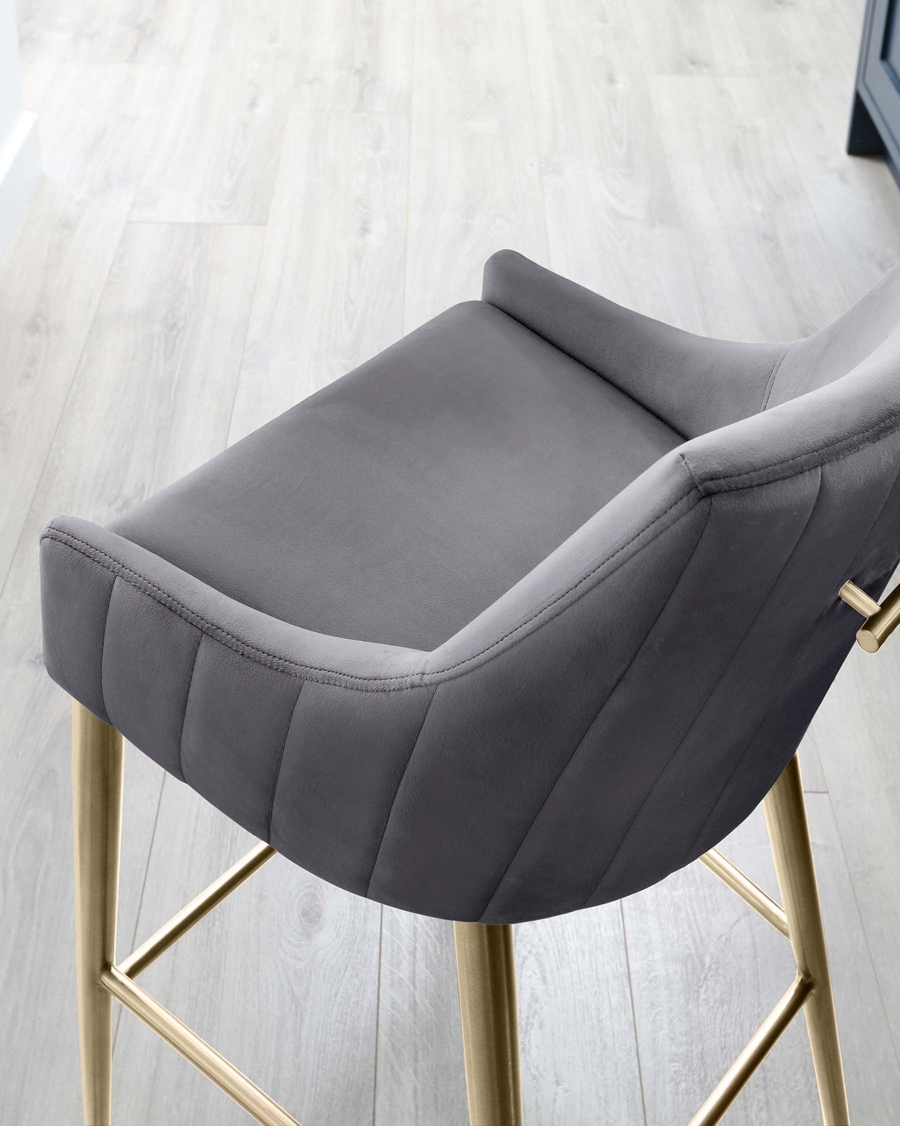 Modern grey upholstered bar stool with a curved backrest and channel tufting detail, featuring sleek gold-finished metal legs with a built-in footrest.