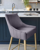 Elegant contemporary barstool with plush, slate grey upholstery and sleek, brass-tone metal legs. Features a high back and armless design, with subtle horizontal channel tufting accents for a modern, sophisticated look. Perfect for kitchen or bar counters.