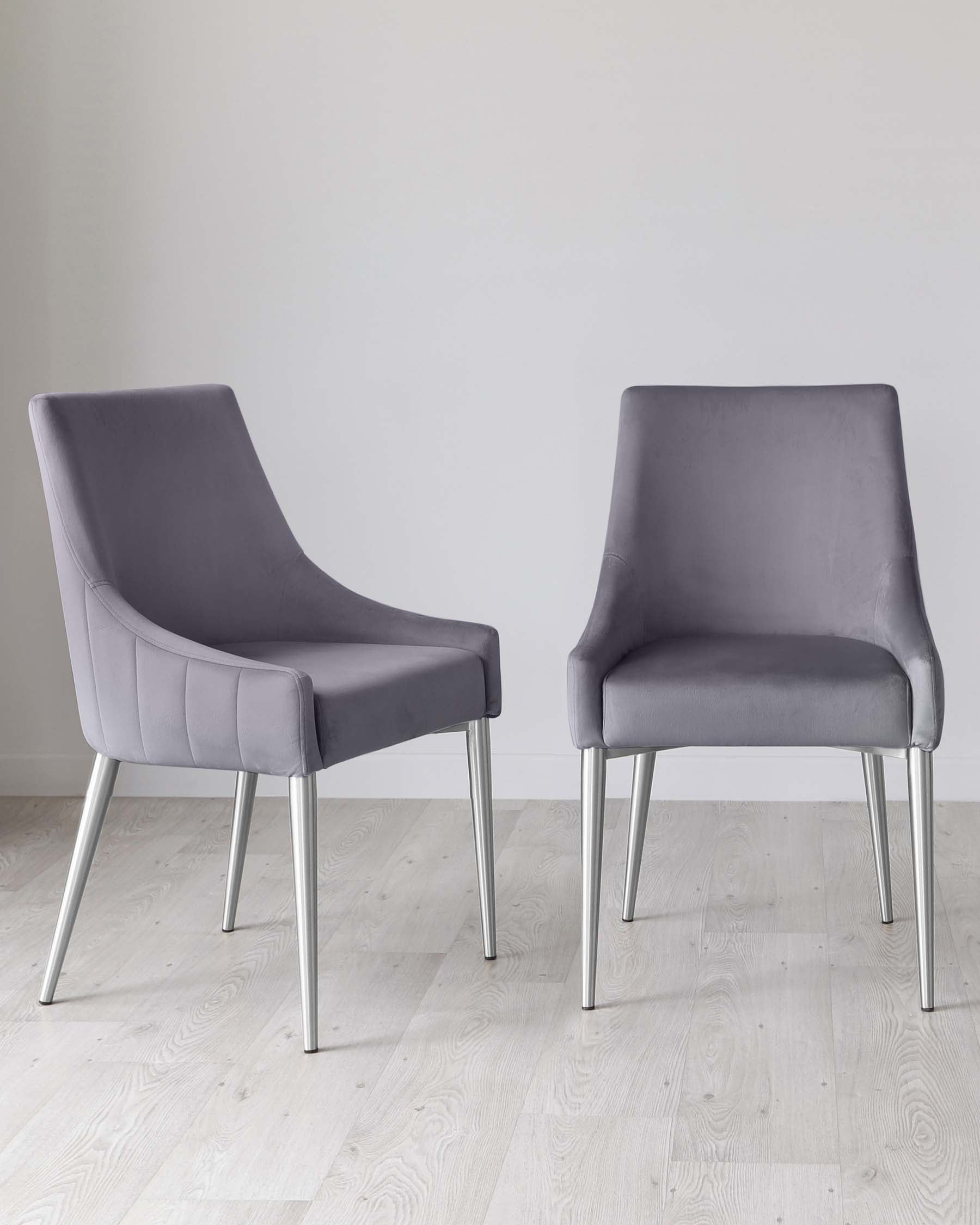 Two modern grey upholstered dining chairs with a sleek design featuring high backs, smooth lines, and four metal legs. The chairs are positioned on a light wooden floor against a neutral wall, suggesting an elegant and contemporary aesthetic.