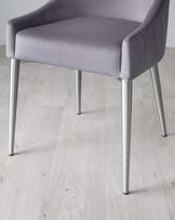 Modern light grey upholstered chair with clean lines, featuring curved armrests and a wide, comfortable seat on sleek, metallic silver legs, set against a light wooden floor for a contemporary look.