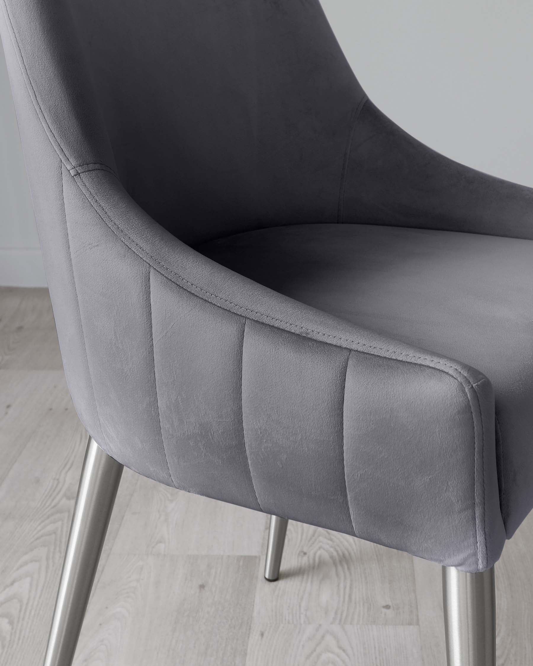 Modern grey upholstered armchair with channel tufting on the backrest and seat, featuring sleek metallic legs. The chair's design offers a blend of comfort and contemporary style, suitable for both living and office spaces.