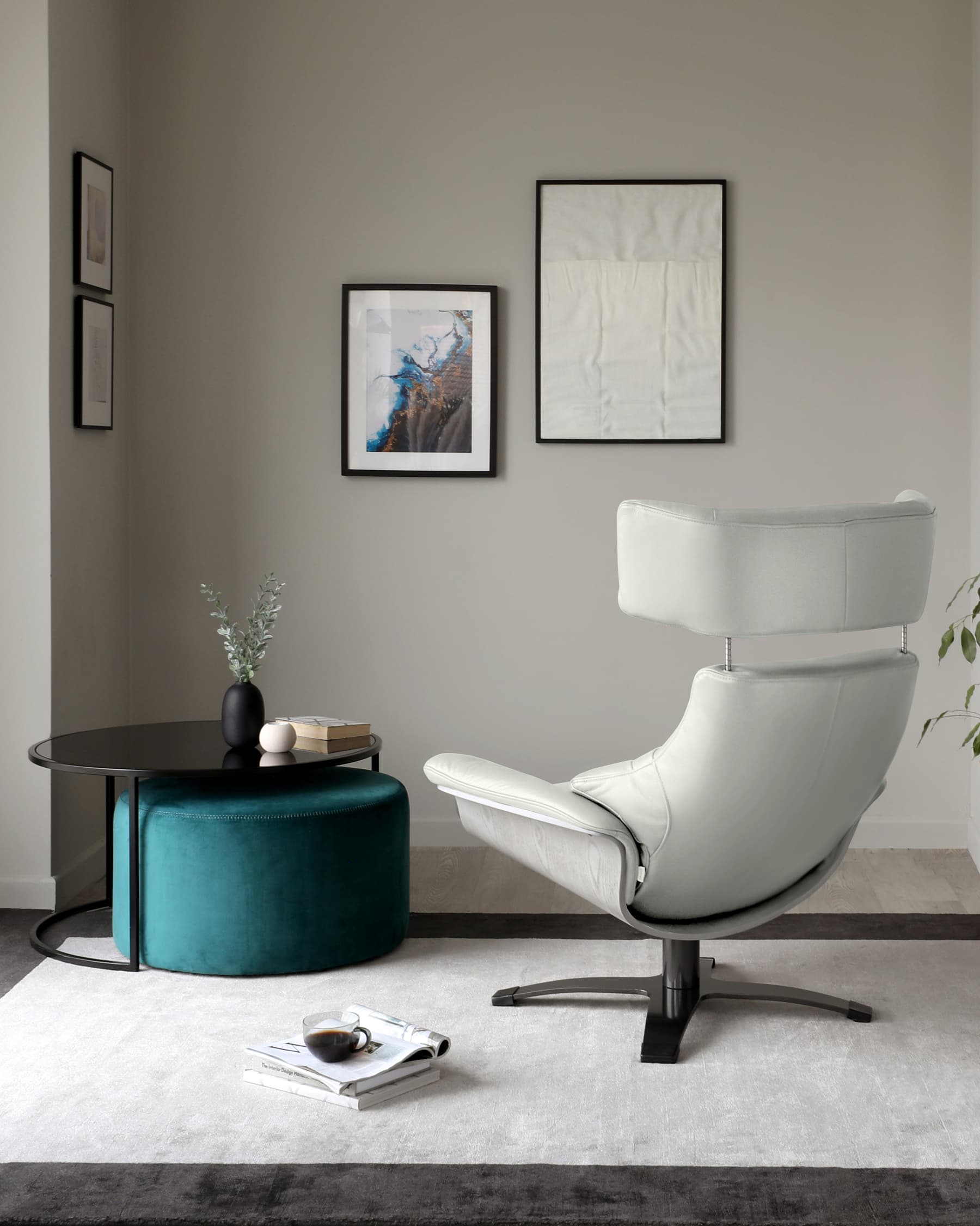 Modern minimalist furniture arrangement featuring a sleek white leather swivel chair with a high back and metal base, a round coffee table with a black top and metal legs, and a luxurious teal velvet ottoman.