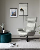 A modern light grey leather lounge chair with a high back and a chrome base, paired with a round black coffee table and a teal ottoman on a textured grey area rug.