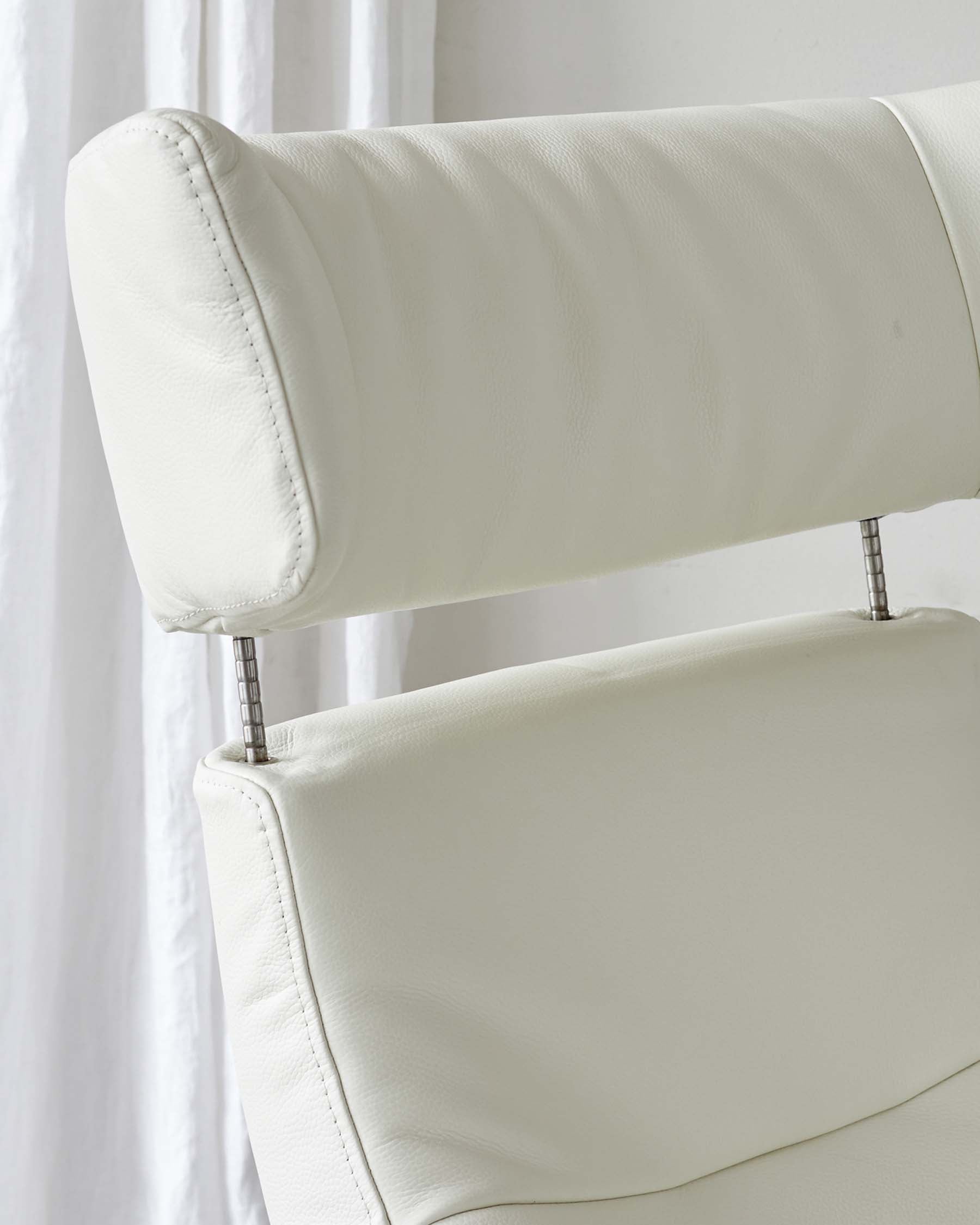 Close-up of a modern white leather chair with detailed stitching and metal accents.