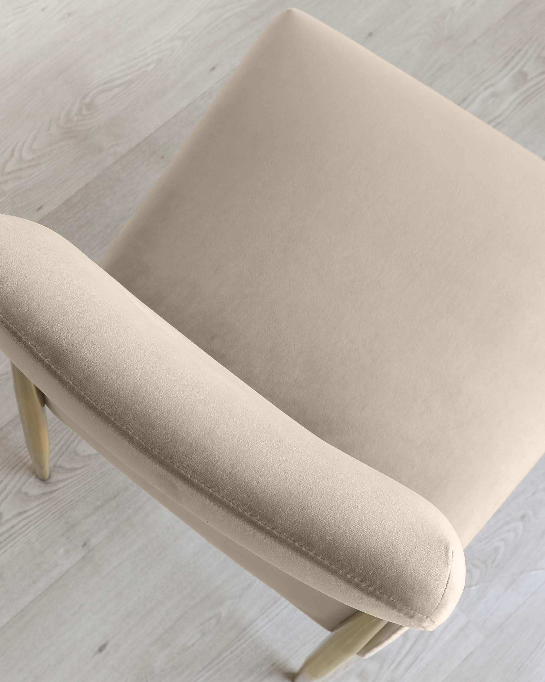 A modern beige upholstered chair with a minimalist design and light wooden legs, set against a light wood floor.