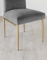 Elegant modern chair with a sleek, high-back design, upholstered in a plush grey velvet fabric. The chair stands on four slender, tapered legs in a polished gold finish, creating a luxurious contrast with the soft texture of the seat.