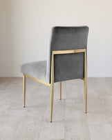 Modern dining chair with a grey velvet upholstery and sleek brass-finished metal legs, set against a neutral background.