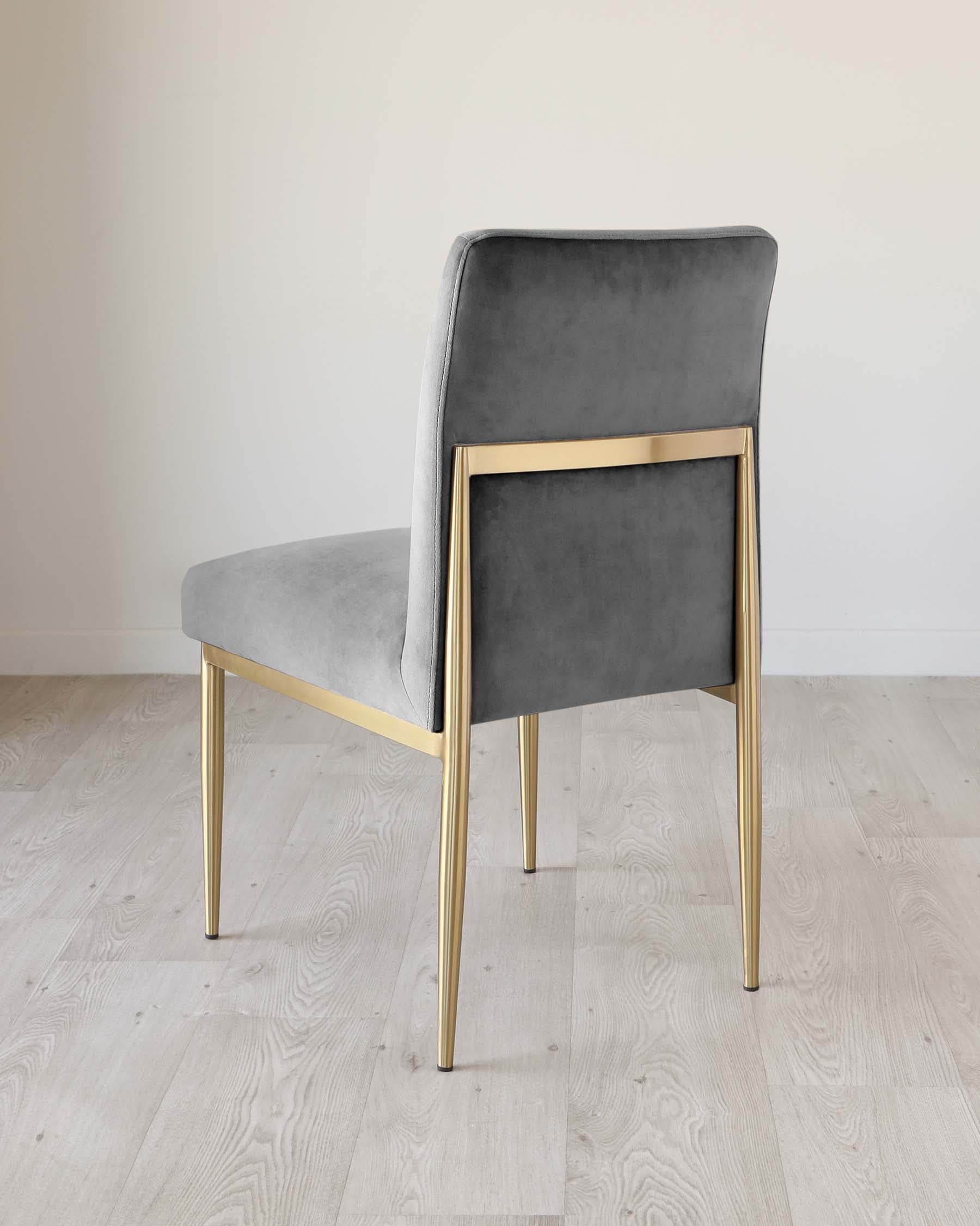 Modern dining chair with a grey velvet upholstery and sleek brass-finished metal legs, set against a neutral background.