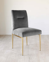 Elegant modern dining chair with a plush, grey velvet upholstery and sleek, tapered gold metal legs. The chair features a subtle, rectangular cut-out on the backrest for a sophisticated design touch.