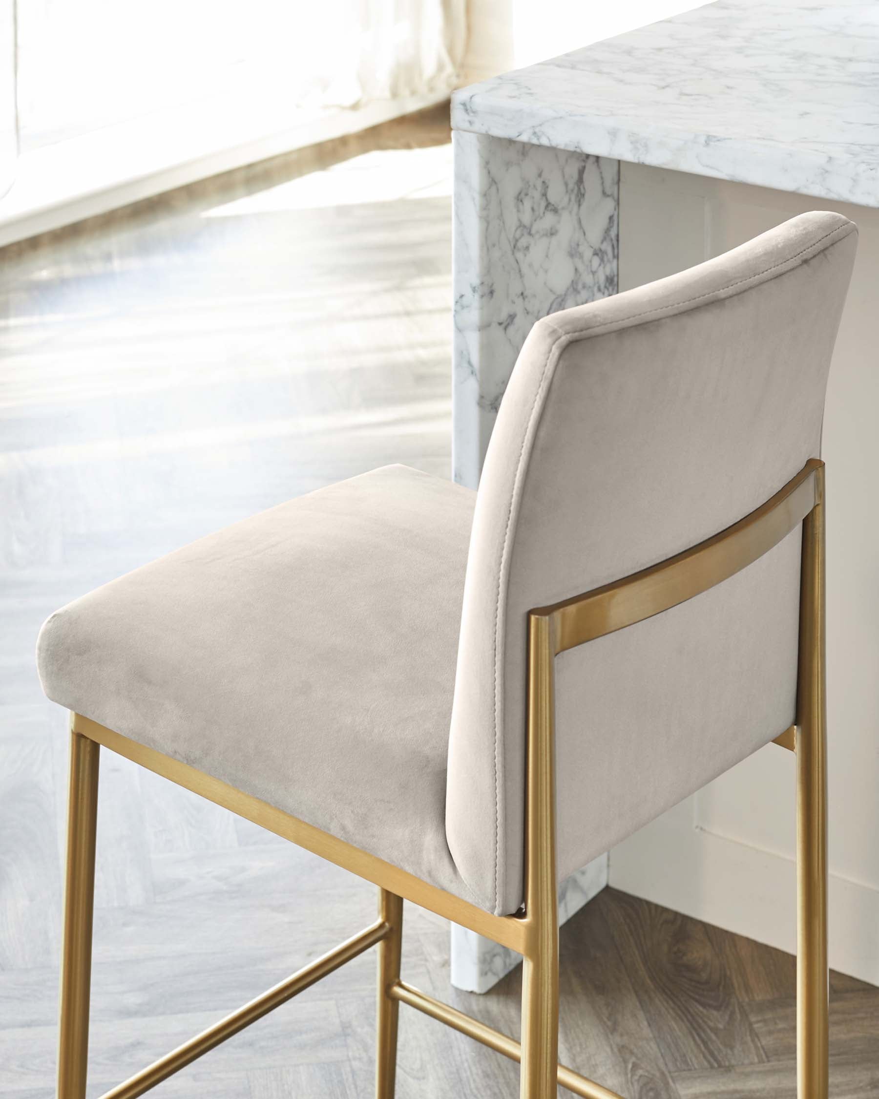 Elegant modern dining chair with a light grey velvet upholstered seat and curved backrest, featuring a sleek gold-finished metal frame, paired with a white marble dining table with prominent grey veining.