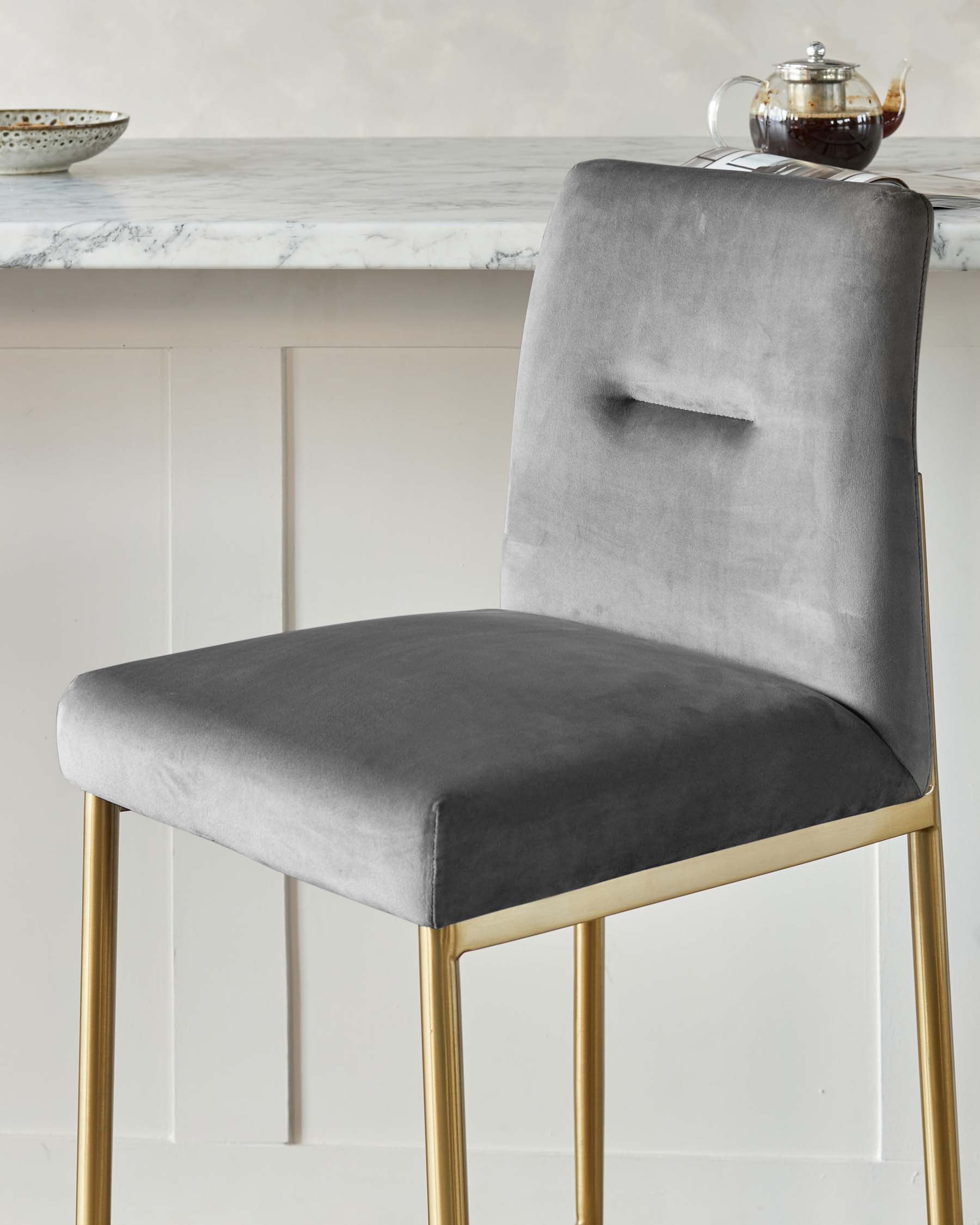 Elegant modern dining chair with a high backrest and plush grey velvet upholstery, featuring a rectangular cut-out detail. The chair stands on sleek, tapered golden metal legs, offering a luxurious and contemporary aesthetic.