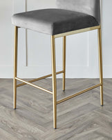 Modern bar stool with a plush, grey velvet seat and a sleek golden metal frame.