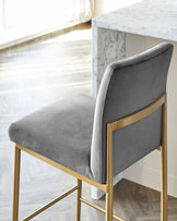 Elegant modern dining chair with grey velvet upholstery and a sleek gold metal frame, positioned next to a white marble-top dining table with a matching gold base.