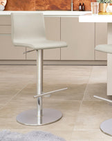 Modern light grey adjustable bar stool with a minimalist design, featuring a sleek chrome pedestal base, attached footrest, and a low-back leatherette seat.