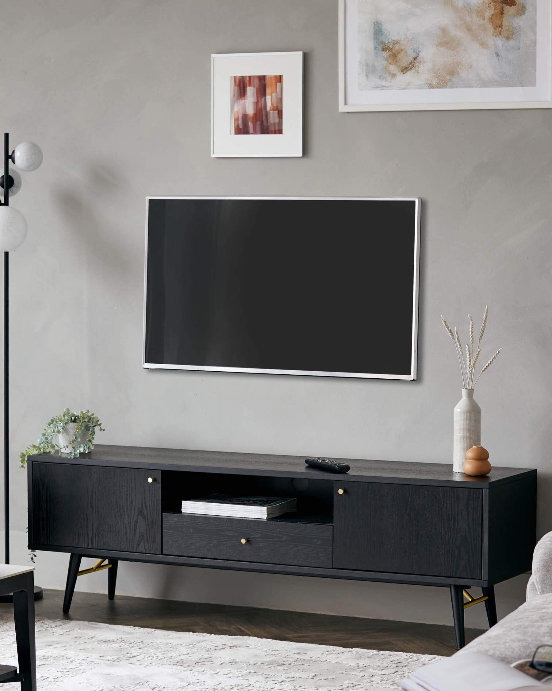 A modern black entertainment centre with gold handles, featuring open shelving and closed cabinets, resting on sleek metal legs.