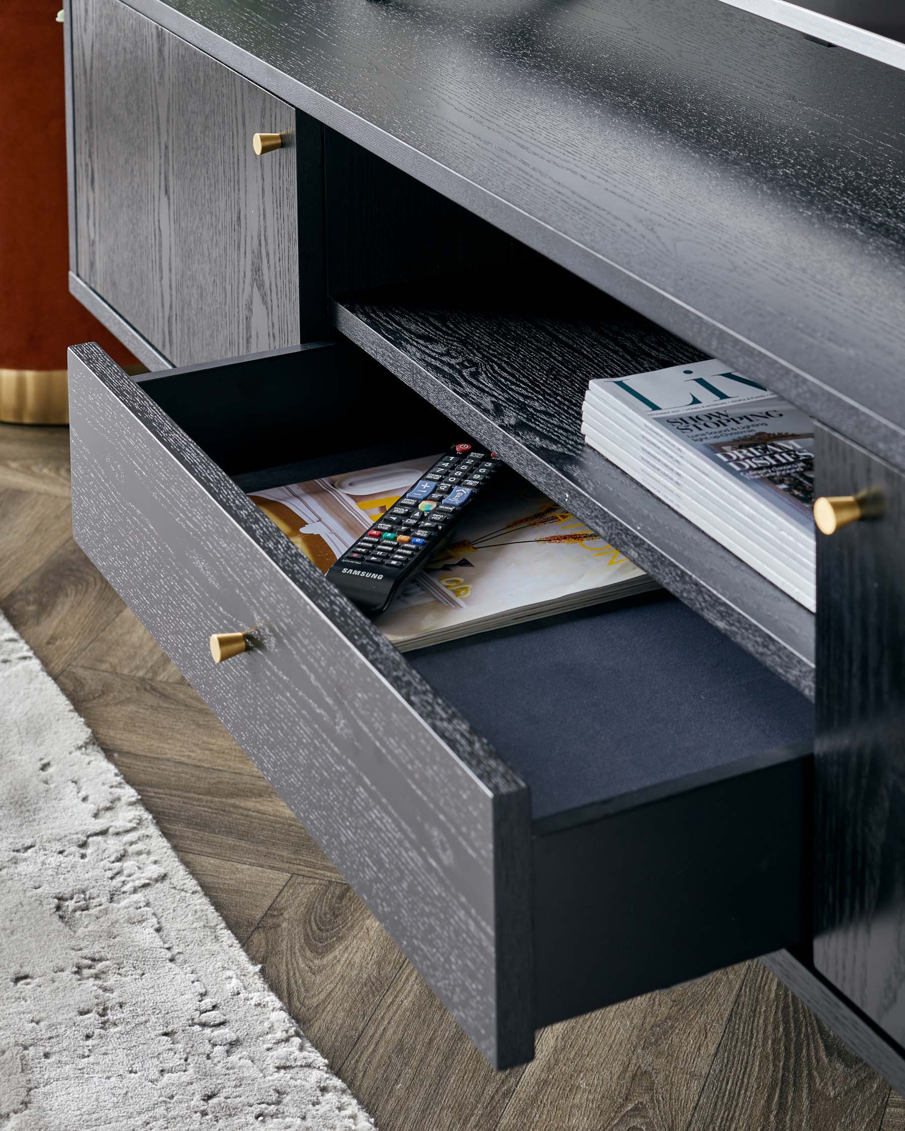 A contemporary dark wood media console with a smooth finish and brass handle accents, featuring an open shelf and partially extended drawer showcasing organized storage space.