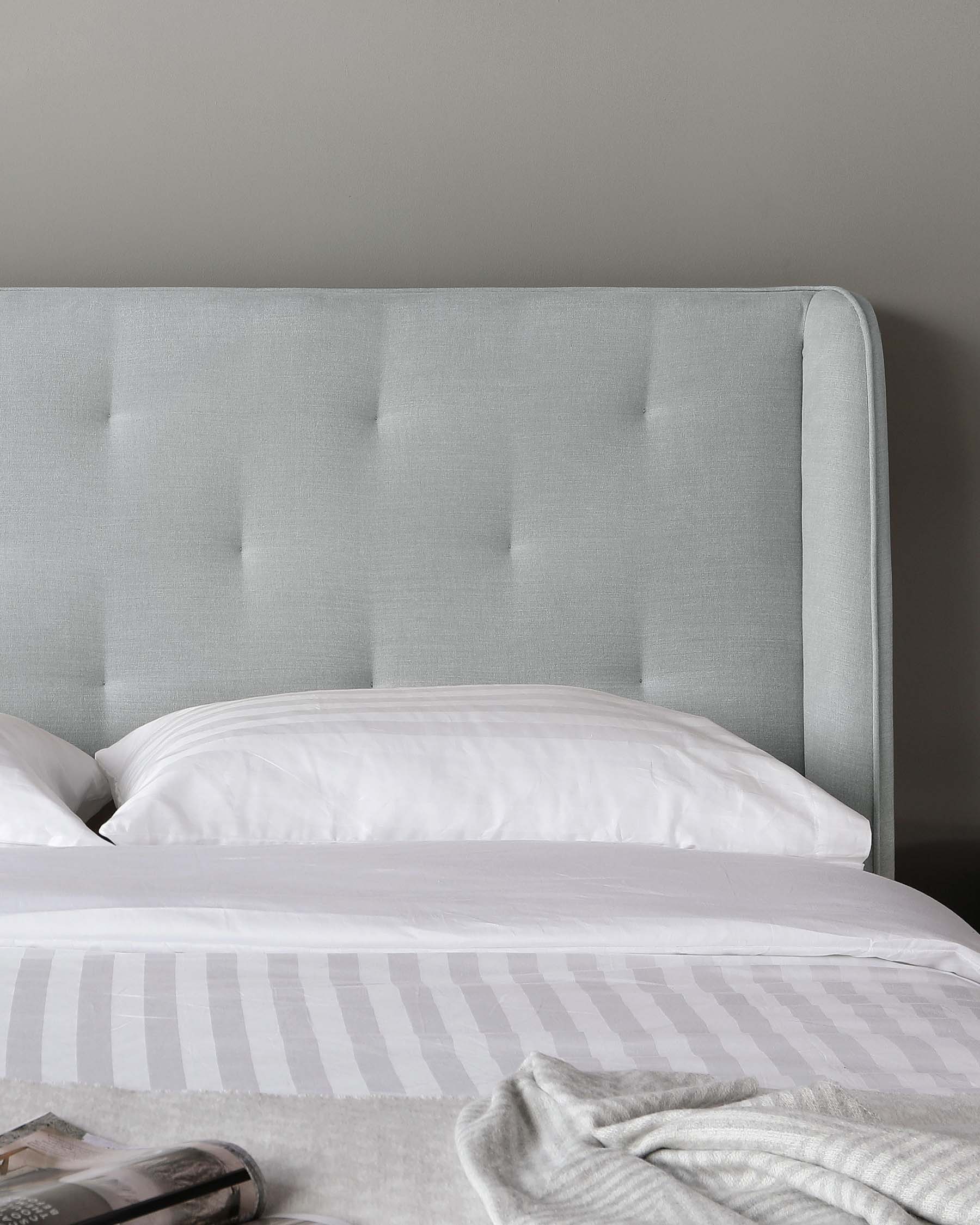 Elegant upholstered headboard in light grey fabric with tufted button accents, accompanying a bed dressed in white and light grey striped bedding.