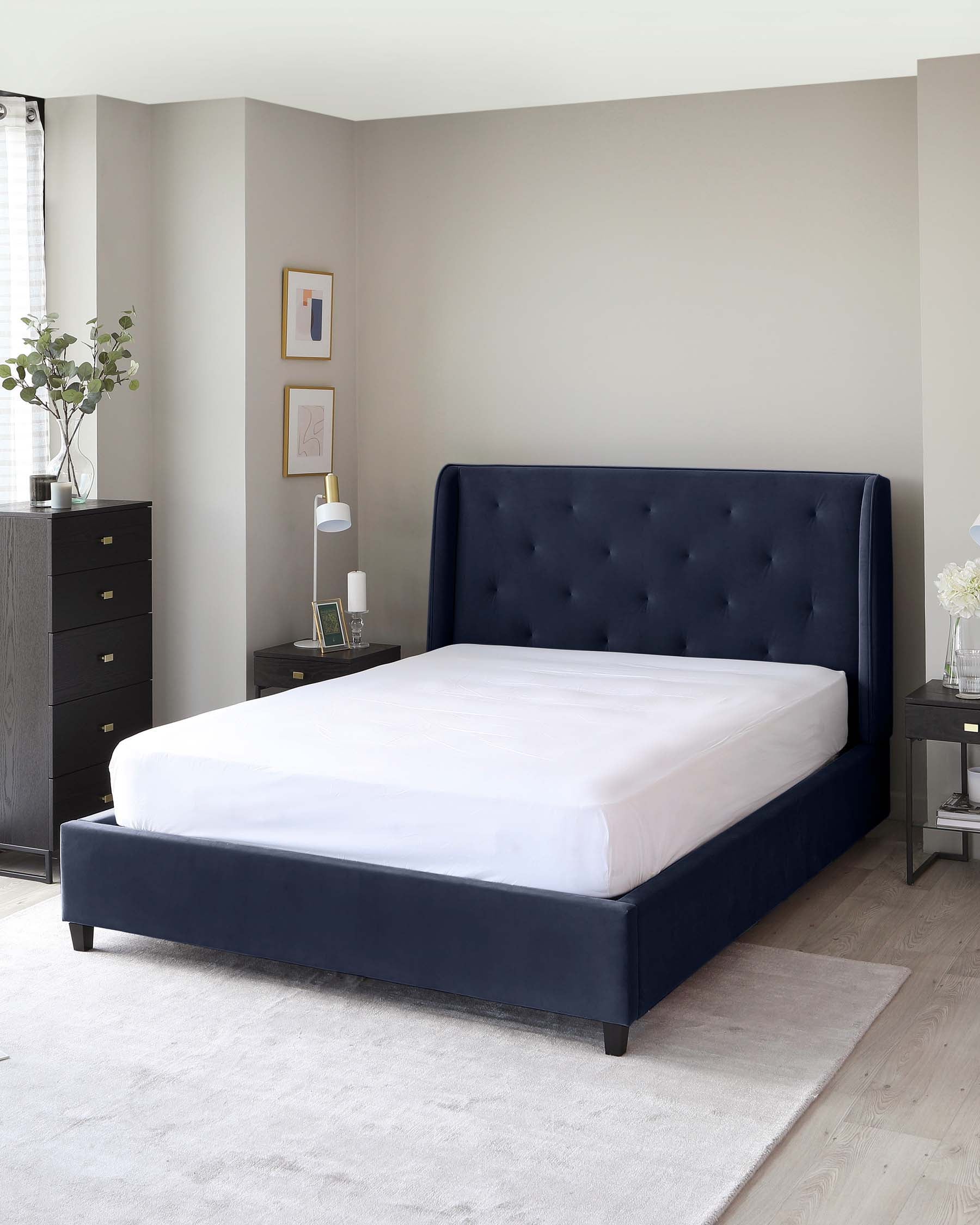 Elegant dark navy upholstered bed with a tufted headboard, a matching footboard, and dark wooden legs, accompanied by a sleek black bedside table with silver handles, and a matching tall black dresser in a contemporary bedroom setting.