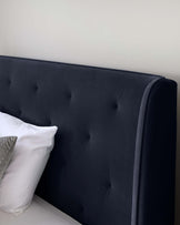 Elegant navy blue upholstered headboard with tufted button detailing and a gently curved top edge, accompanied by white and grey decorative pillows.