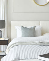 Modern bedroom with a minimalist design featuring an upholstered off-white headboard, a sleek black bedside table with an open shelf and a single drawer, topped with a contemporary grey lamp.