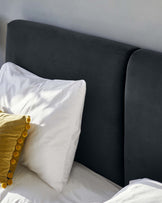 Elegant modern bed with a smooth, dark grey upholstered headboard, complemented with crisp white bedding and a decorative mustard pillow with pom-pom details.