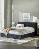 Modern bedroom with a low-profile upholstered platform bed in dark blue, paired with matching nightstands, white cylindrical table lamps, and a textured area rug.