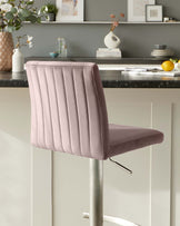 Modern blush pink bar stool with vertical channel tufting, plush seat, and a sleek chrome base with a footrest.