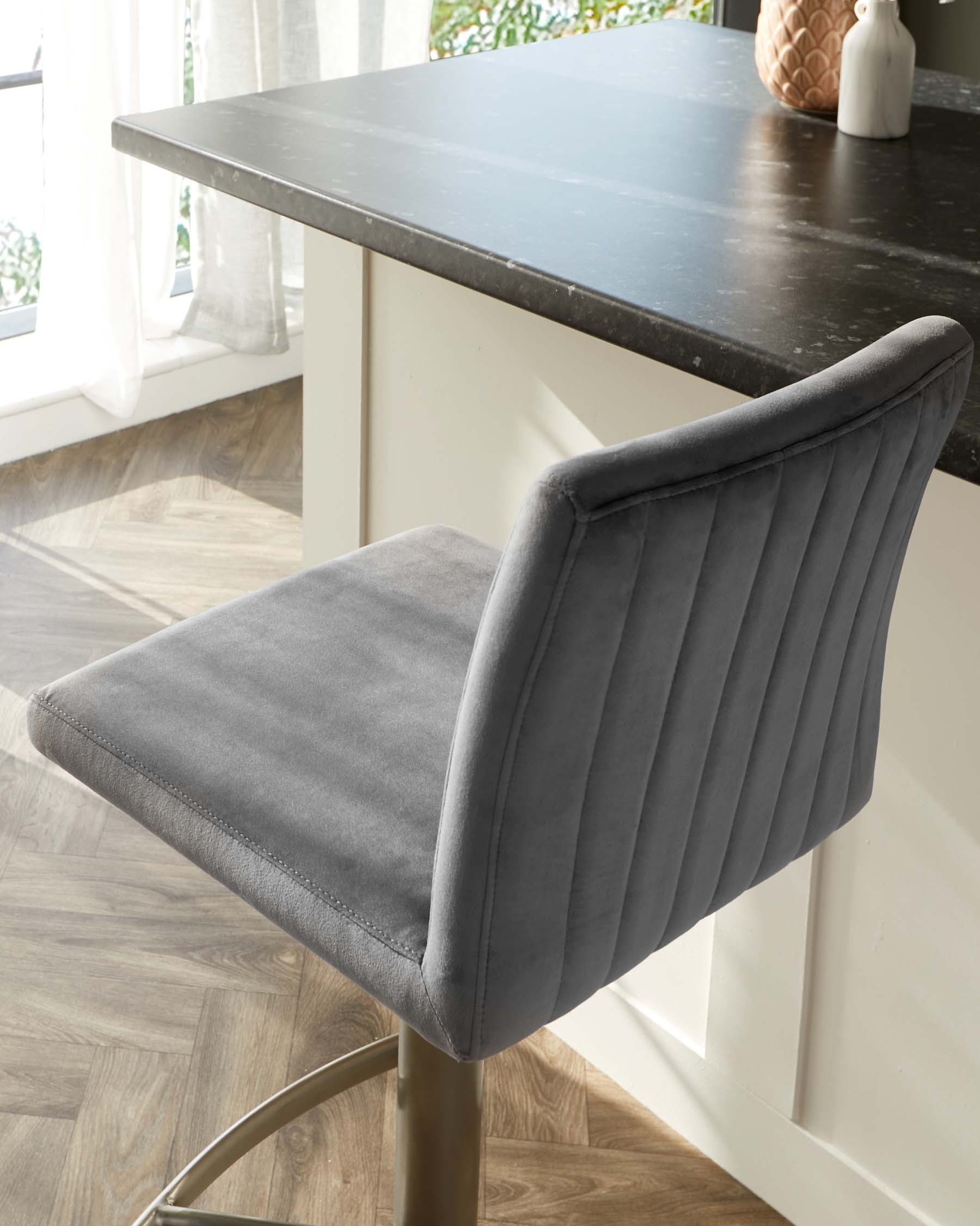 Contemporary grey upholstered dining chair with vertical channel tufting and a curved backrest, paired with a modern dark stone tabletop with a white finished base. Visible accessories include a decorative vase and a small figurine.