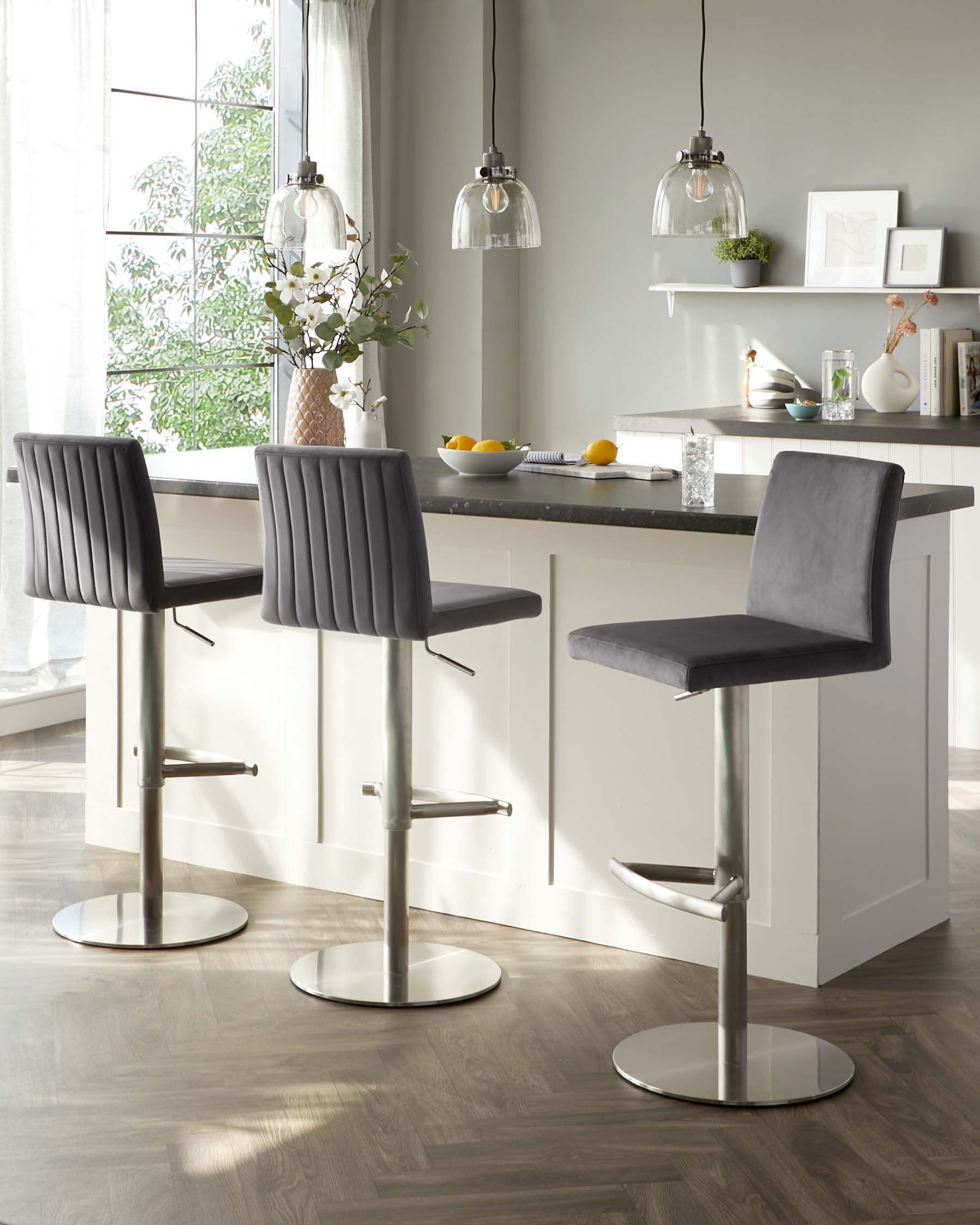 Modern adjustable height bar stools with grey upholstered seats and horizontal channel stitching, chrome pedestal bases, and built-in footrests, paired with a white countertop bar table.