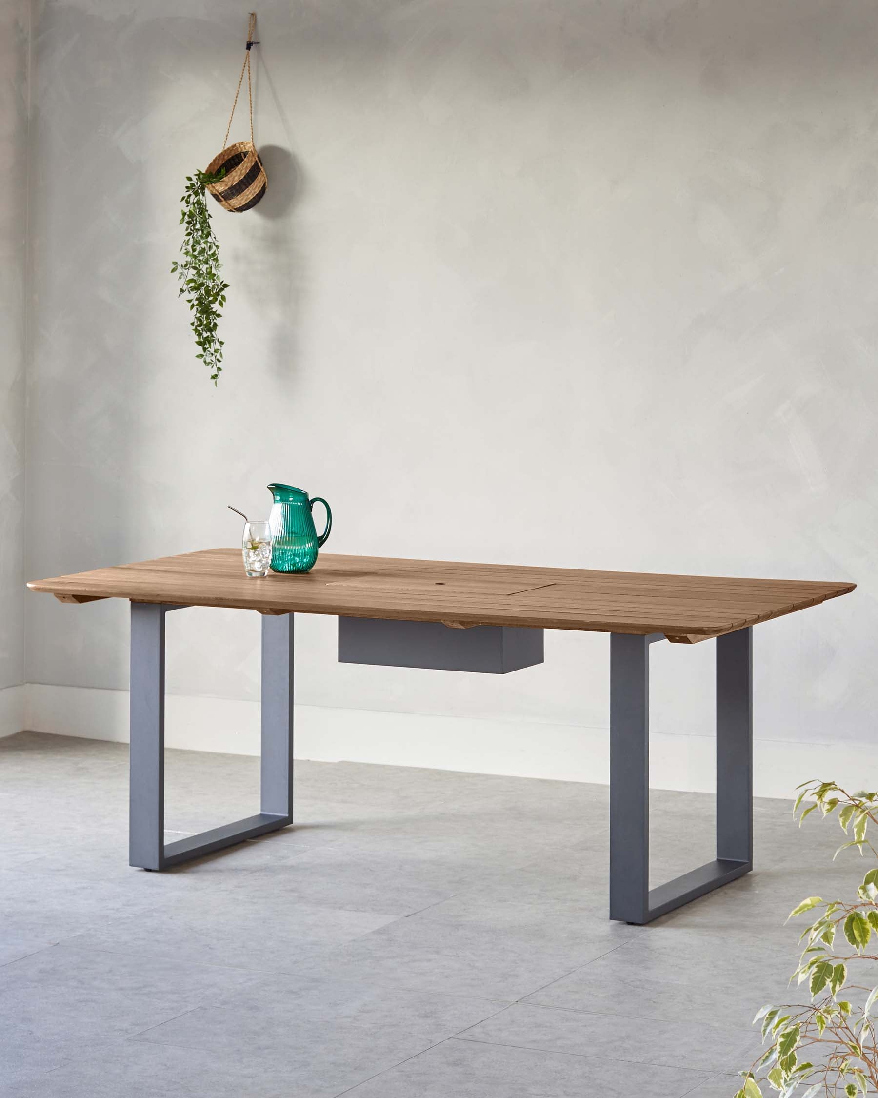 A stylish wooden dining table with a sleek gray metal base, featuring a minimalist drawer and surrounded by greenery.