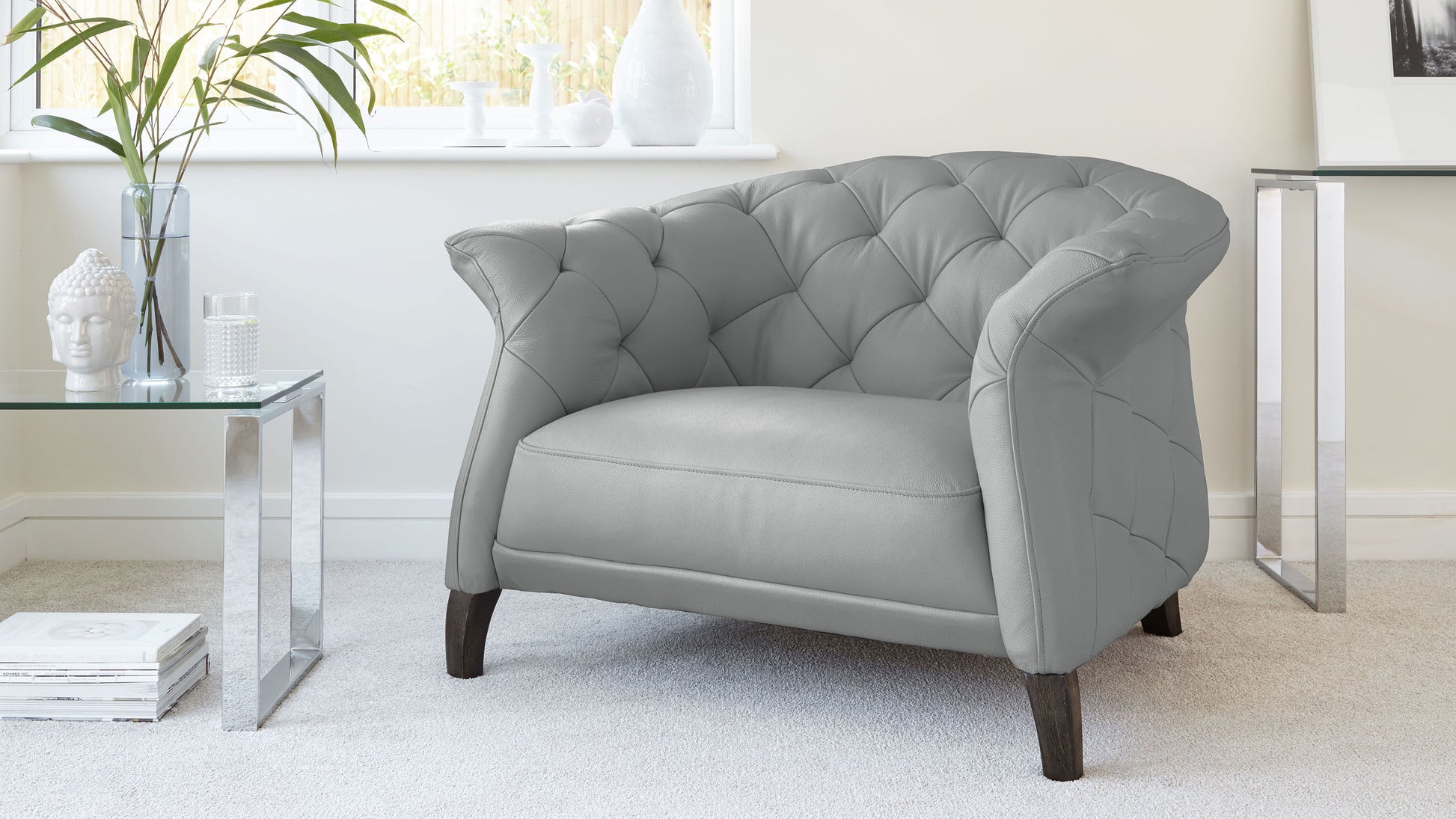 Elegant light grey tufted accent chair with dark wooden legs, paired with a modern clear glass side table with polished chrome legs.