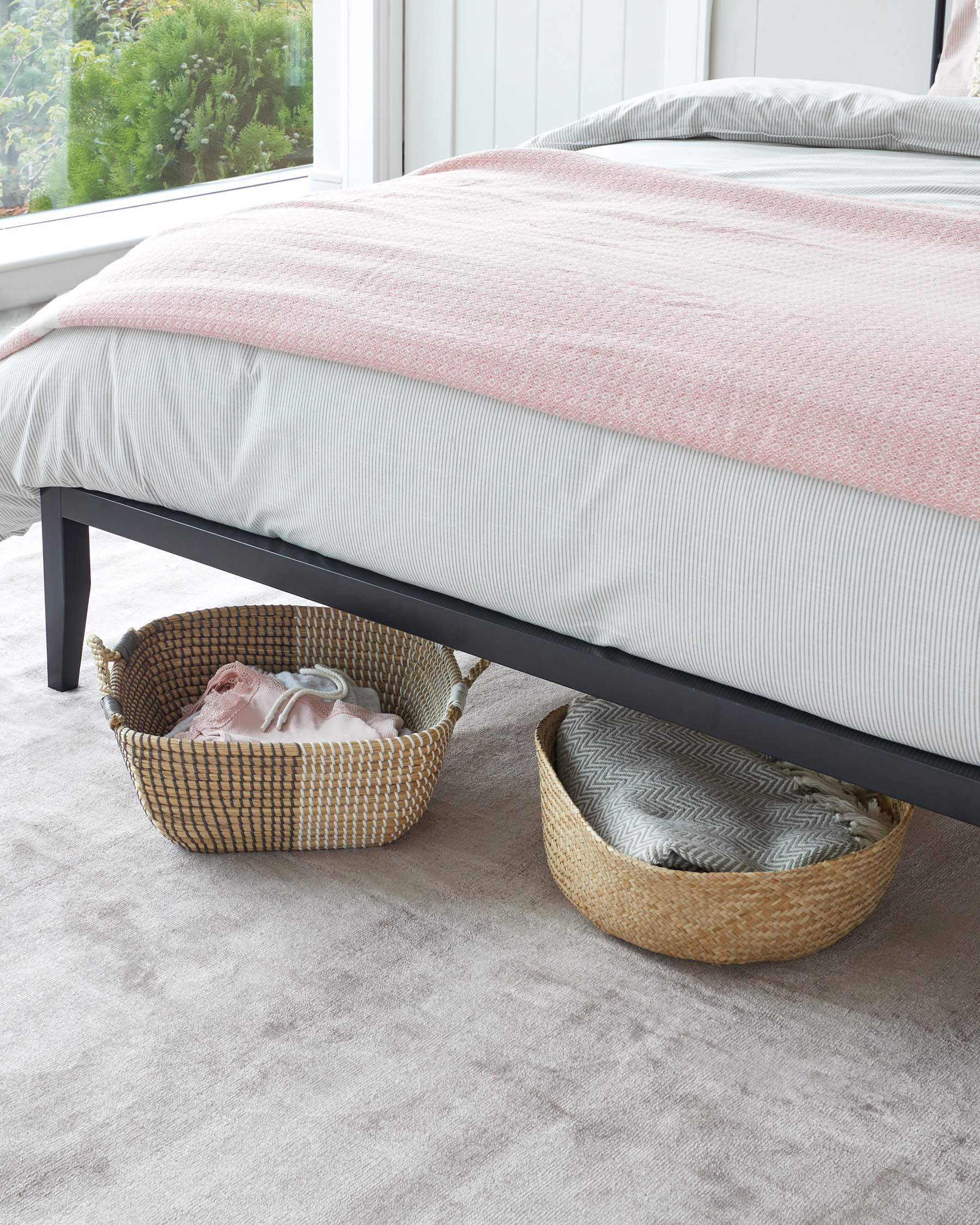 Modern minimalist-style platform bed with a matte black metal frame, accompanied by two woven natural fibre storage baskets placed under the bed.