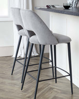 Two modern bar stools with light grey fabric upholstery and sleek black metal legs set against a kitchen counter.