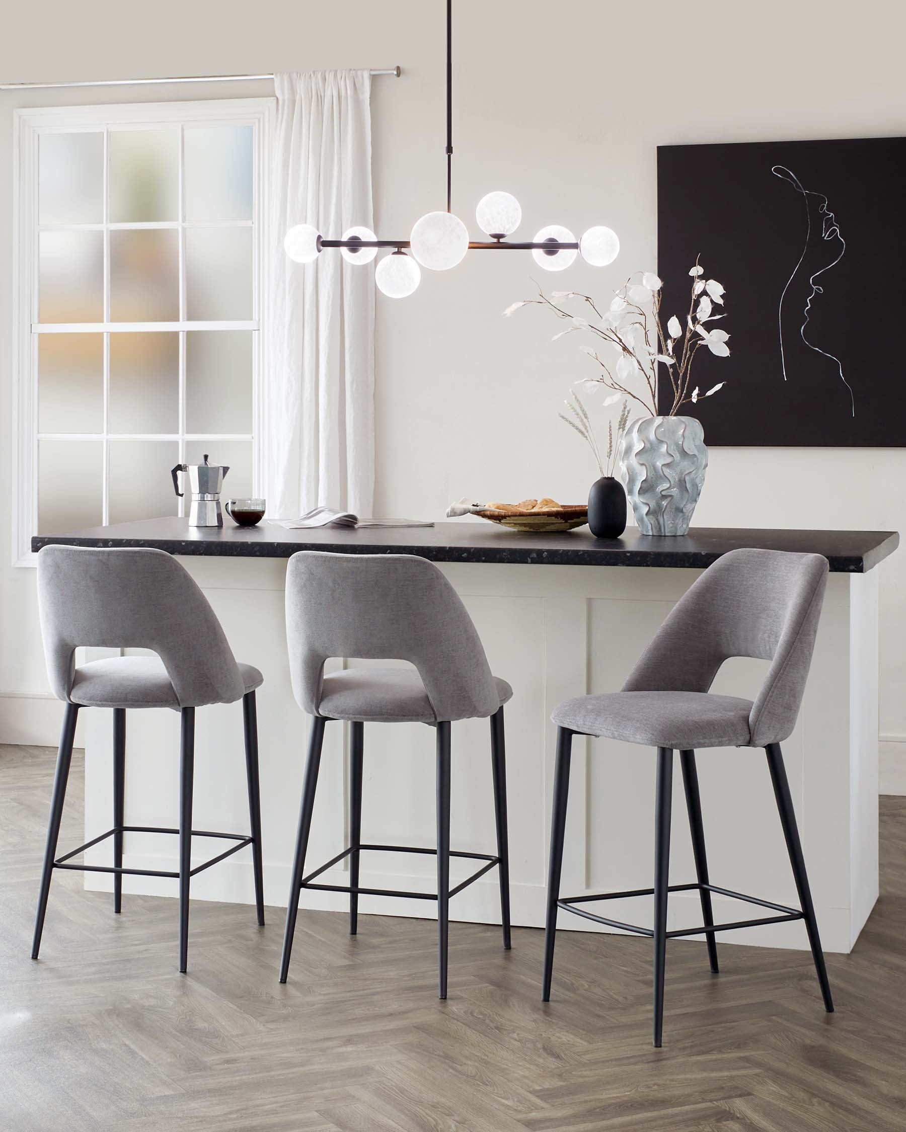 Modern kitchen with three upholstered counter-height bar stools featuring rounded backrests and slender metal legs in black finish, positioned by a kitchen island with a dark countertop.