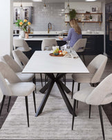 Modern rectangular white marble-top dining table with black angular legs surrounded by six light grey upholstered dining chairs with tapered black legs, set on a textured grey area rug.