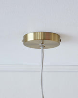 Modern brass flush mount ceiling fixture with a simple circular design and a textured white fabric-covered cord.