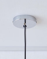 There is no furniture visible in this image. The image displays a minimalist-style ceiling lamp installation with a silver finish canopy mounted on a white ceiling, and a black electrical cord running vertically down from it.