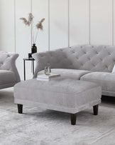 Gray upholstered sofas with tufted backs, a matching ottoman, and a sleek black side table with decorative elements.