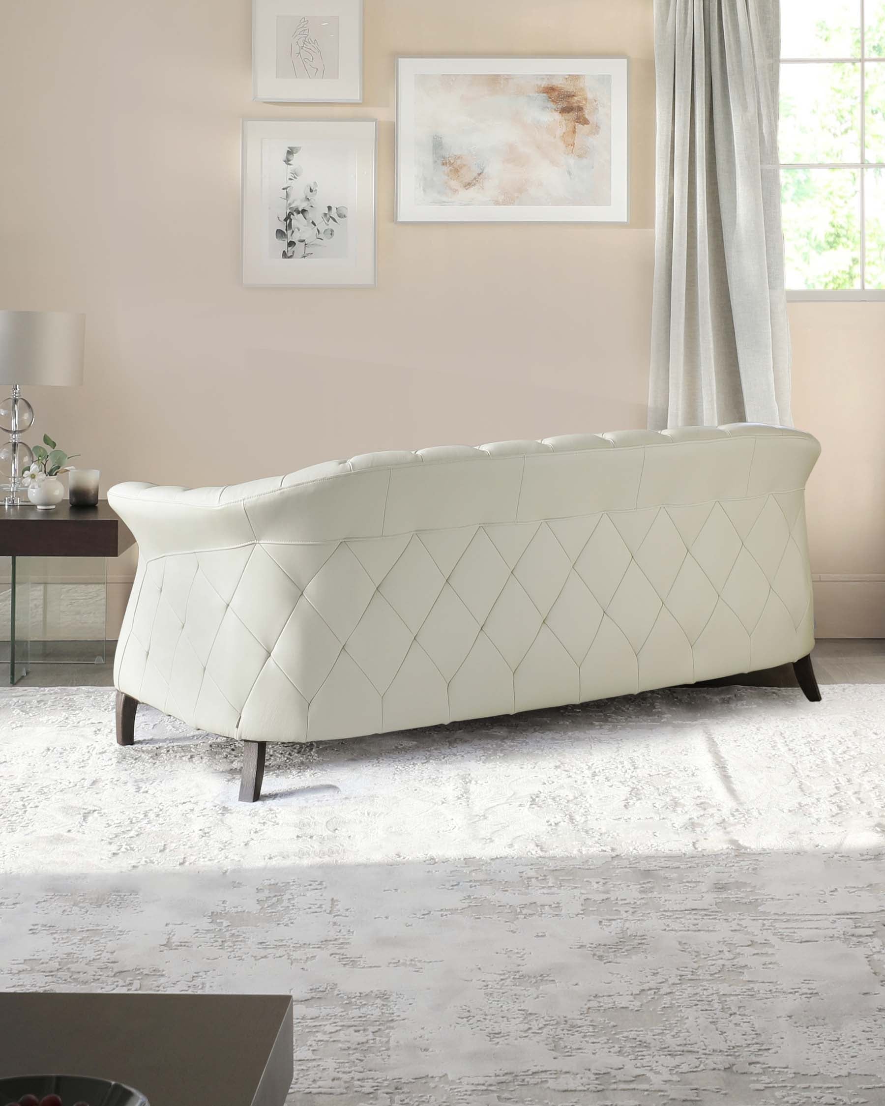 Elegant, curved white tufted loveseat with a diamond pattern design and dark wooden legs, set in a cosy room with neutral tones and tasteful wall art.