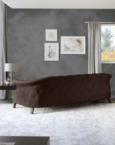 Elegant dark brown leather sofa with a geometric quilted pattern on the backrest, complemented by a sleek black end table with a stylish table lamp featuring a silver base and a white shade, set against a modern grey backdrop.