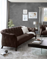 Elegant brown tufted leather sofa with matching armchair, complemented by a glass-top coffee table with dark wooden base, set against a distressed white rug.