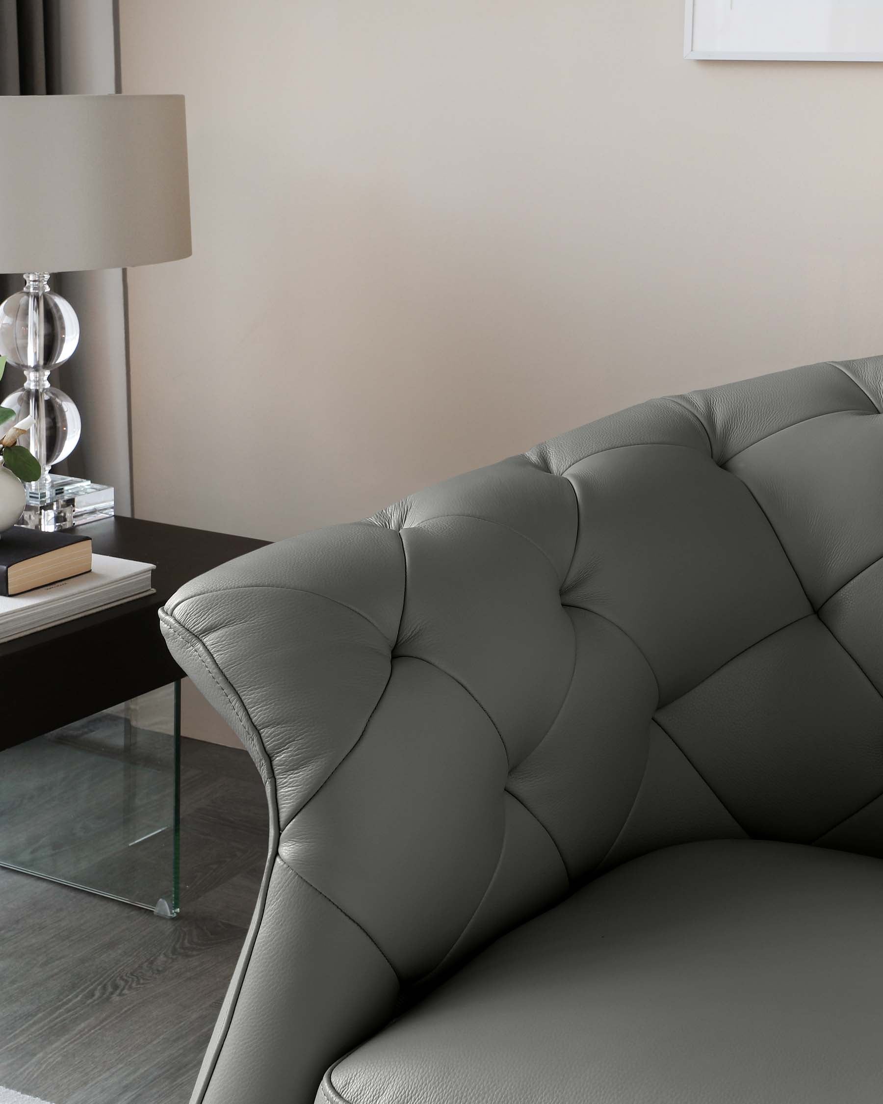 Elegant grey tufted leather sofa with a modern glass side table featuring a contemporary lamp and decorative accessories.