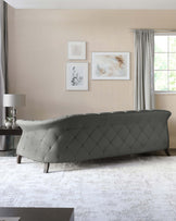 Elegant modern tufted bench with a curved silhouette and refined diamond stitching detail, upholstered in a tasteful grey fabric, supported by dark tapered wooden legs, showcased in a chic interior with a neutral colour palette.