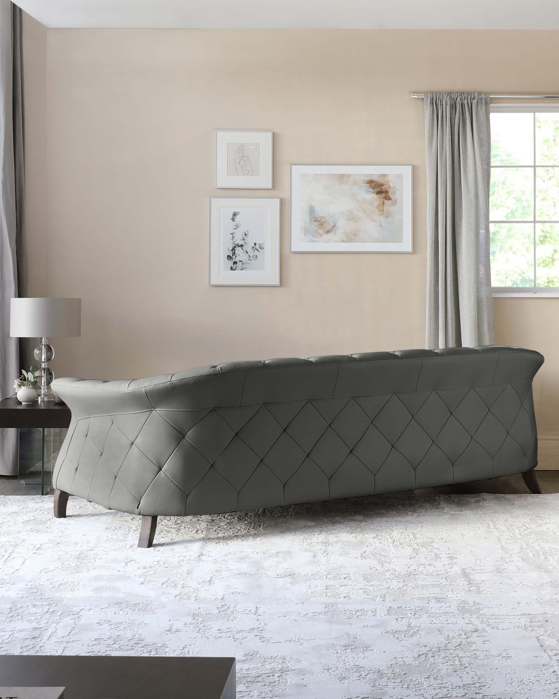 Elegant modern tufted bench with a curved silhouette and refined diamond stitching detail, upholstered in a tasteful grey fabric, supported by dark tapered wooden legs, showcased in a chic interior with a neutral colour palette.