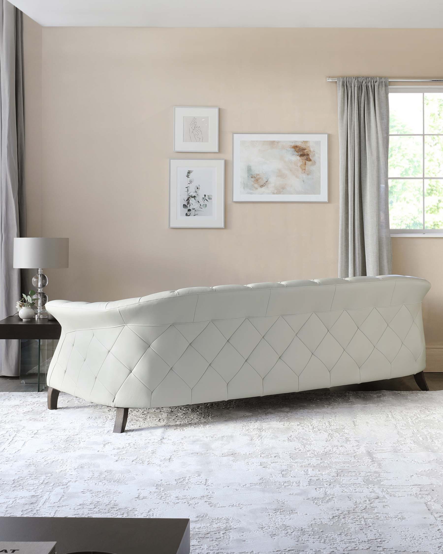 Elegant modern light grey upholstered sofa with a curved backrest and geometric tufting details, supported by dark wooden legs, in a contemporary living room setting with neutral colour tones and soft-textured décor.