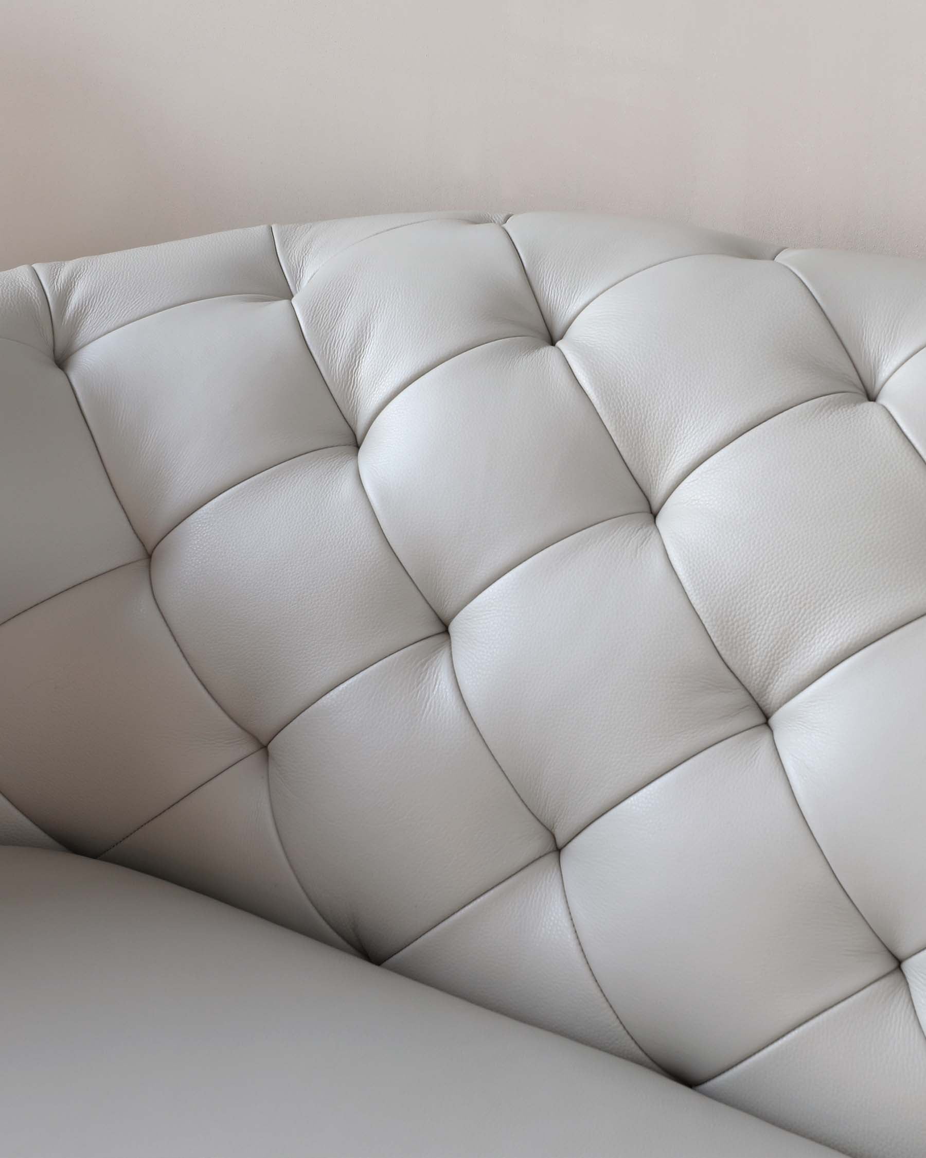 Close-up view of a white leather tufted sofa, displaying the quilted pattern and plush cushioning.