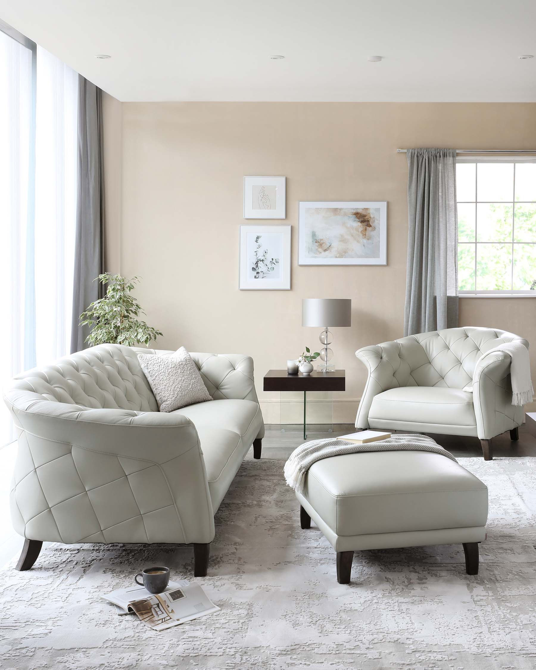 Elegant living room set featuring a quilted ivory leather sofa, matching armchair, and ottoman, all with dark wooden legs. A small side table with dark finish and a grey table lamp is positioned to the right. The arrangement rests on a textured light grey area rug, and decorative pillows add a touch of contrast.