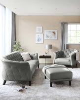 A contemporary living room set featuring a plush, tufted, light grey leather sofa and a matching armchair with quilted detailing. Between them stands a small square, dark-stained wooden coffee table with a glass vase and a pair of modern table lamps. To the right, a coordinating ottoman complements the set, draped with a soft white throw blanket.