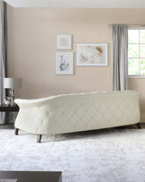 Elegant cream tufted sofa with a curved back design and diamond stitching patterns on the upholstery, set against a neutral-toned wall, finished with dark wooden legs.