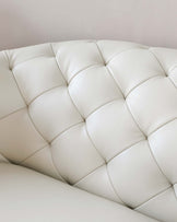 Close-up of a cream-colored leather sofa featuring a tufted design with plump, quilted cushions.